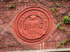 an emblem on the side of a red brick building with vines growing around it,