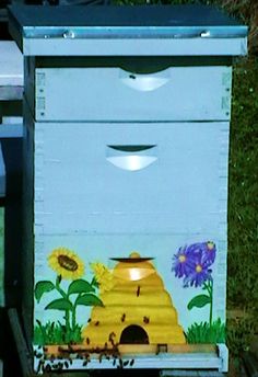 a beehive painted with sunflowers and bees on the outside, in front of some grass