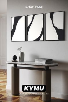 two black and white paintings hanging on the wall above a console table with vases