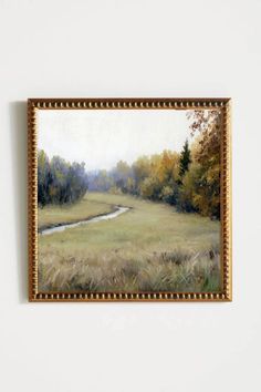 a painting hanging on the wall next to a white wall with a brown frame and a river running through it