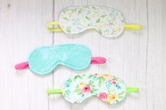 three eye masks with flowers on them are lined up against a white wooden background,