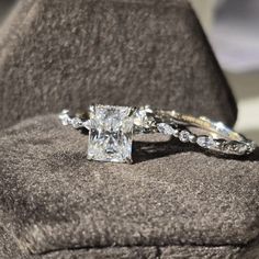 an engagement ring with a princess cut diamond in the center on a cushioned surface