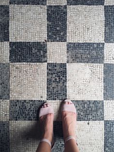 a woman's feet in sandals standing on a checkered tile floor