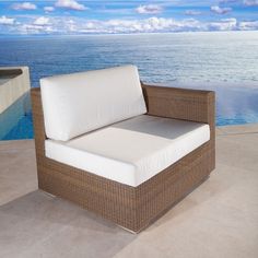 a wicker chair with white cushions next to a pool and the ocean in the background