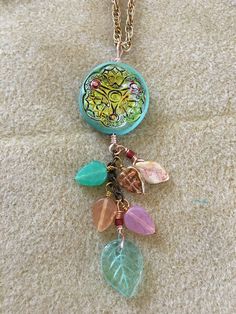 This is a two sided clay pendant with multiple Czech glass leaves that cascade from the bottom of the pendant. The chain is gold plated and is 24 inches long. Gold Necklaces With Nickel Free Czech Glass, Bohemian Green Necklaces With Charms, Bohemian Green Necklace With Charms, Gold Czech Glass Pendant Necklace, Green Bohemian Pendant Charm Necklace, Gold Nickel-free Necklace With Czech Glass, Gold Nickel-free Czech Glass Necklaces, Czech Glass, Gold Plate