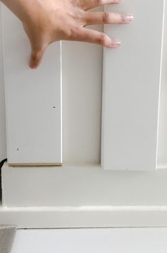 a person's hand reaching out from behind a door handle on a white cabinet