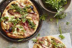 two pizzas with different toppings sitting on top of a table next to bowls of salad