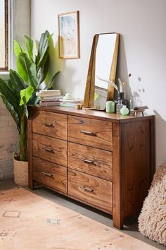 a room with a dresser, mirror and plant in it on the floor next to a window