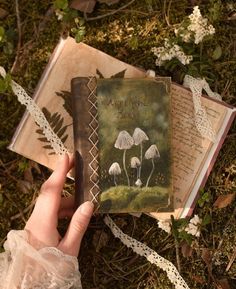 a person holding an open book in their hand on the ground with flowers and grass