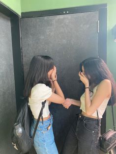 two young women standing next to each other in front of a black wall and holding hands