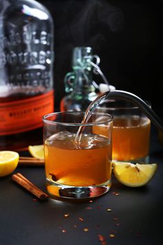 a glass filled with liquid next to two lemons and cinnamon sticks on a table