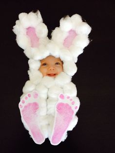 a baby in a bunny costume with pink feet and white fluffy hair is looking up at the camera