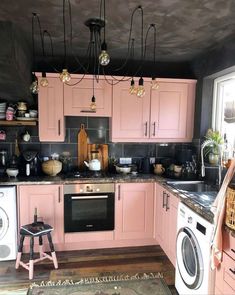 a kitchen with pink cabinets and black counter tops is pictured in this image, there are washing machines on the floor next to the sink