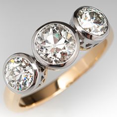 three stone diamond ring in yellow gold and white gold with diamonds on the sides, set against a grey background