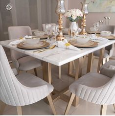 a dining room table is set with white dishes and gold place settings