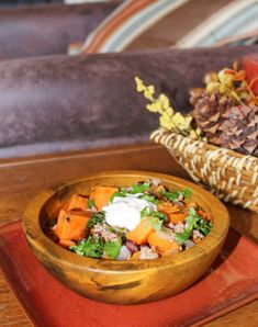 a wooden bowl filled with food sitting on top of a red place mat next to a pine cone