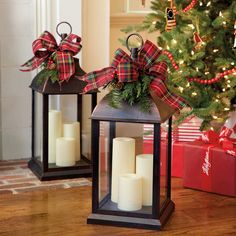 two christmas lanterns with bows and candles in front of a christmas tree on the floor