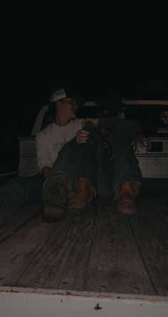 a man sitting on the back of a truck at night with his feet up in the air