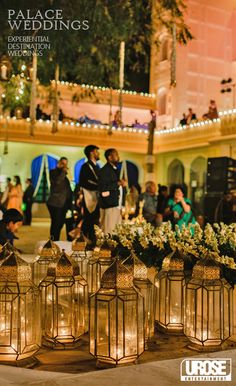 many lanterns are lined up on the ground with flowers in them and people standing around