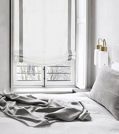 an unmade bed in front of a window with white sheets and pillows on it