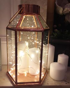 two candles are lit in a glass lantern with fairy lights on the inside and outside