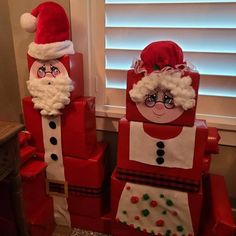 two santa claus made out of cardboard boxes sitting next to each other in front of a window