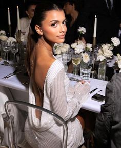 a beautiful woman sitting at a table in front of some candles and flowers on it