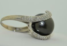 This is an impressively large pearl ring. The pearl is a south Sea Black Tahitian Pearl. The pearl is drilled and mounted with pave diamond accents. The small prong is drilled on the side and the fingers of diamonds are securing the pearl with no movement. This pearl is big, measuring in at 15.5 mm. It is a deep grey/black, perfectly round. There are a couple of natural dimples on the side not the top of the pearl as photographed The setting is 14K White gold, not hallmarked but tested and guara Formal Black Tahitian Pearl Ring, Tahitian Pearl Ring With Diamond Accents Fine Jewelry, Classic Tahitian Pearl Ring With Diamond Accents, Fine Jewelry Tahitian Pearl Ring With Diamond Accents, Tahitian Pearl Ring With Diamond Accents, Luxury Tahitian Pearl Ring With Diamond Accents, Elegant Tahitian Pearl Ring With Diamond Accents, Black Luxury Pearl Ring For Formal Occasions, Formal Tahitian Pearl Ring With Diamond Accents