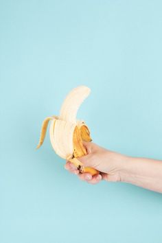 a person holding a half peeled banana in their left hand on a blue background with copy space