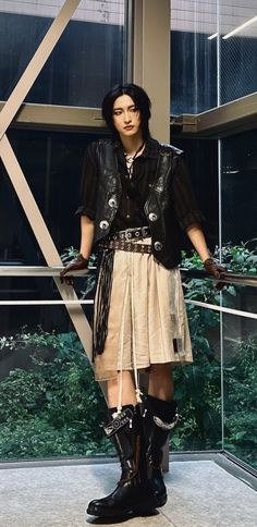 a woman standing in front of a window wearing black boots and a skirt with chains on it