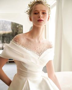 a woman in a white wedding dress standing next to a window with her hands on her hips