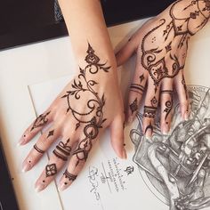 two hands with henna tattoos on them sitting next to a drawing pad and pen