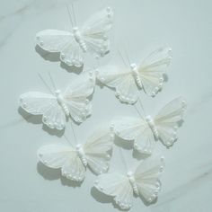 four white butterflies with pearls on them sitting next to each other in the middle of a marble surface