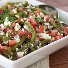 a white bowl filled with green beans and feta cheese on top of a wooden table