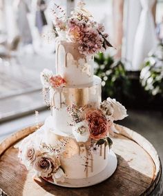 a three tiered wedding cake on top of a wooden barrel with flowers and greenery