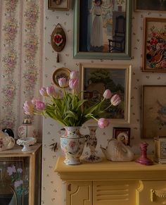 a vase filled with pink flowers sitting on top of a yellow dresser next to pictures