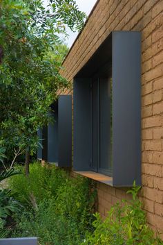 an open window on the side of a brick building with green plants growing around it