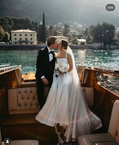 a bride and groom kissing on the back of a boat in front of a lake