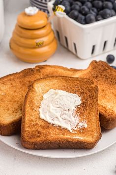 two pieces of toast on a plate with butter and blueberries in the background,