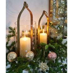 two lit candles sitting on top of a christmas wreath with evergreen branches and ornaments around it