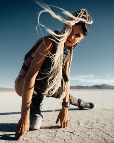 a woman with long hair crouches down in the desert