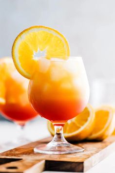 two glasses filled with orange juice and garnished with lemons on a cutting board