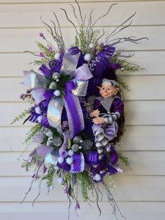 a purple and silver wreath hanging on the side of a house with a doll in it