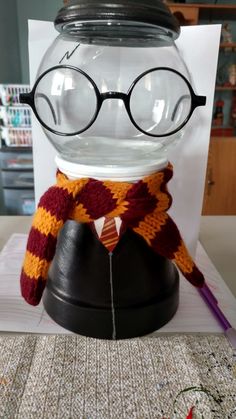 a glass fish bowl with glasses and a scarf on it's head, sitting on top of a table