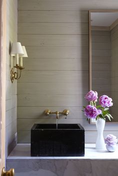 a bathroom with a sink, mirror and flowers in the vase on the window sill