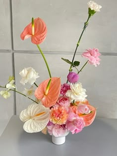 a white vase filled with flowers on top of a gray table next to a tiled wall