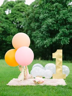 a table topped with balloons next to a number one sign on top of a grass covered field