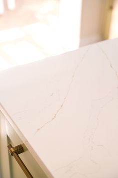 a white marble counter top in a kitchen with gold handles and knobs on it