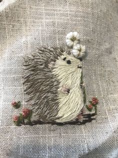 an embroidered hedgehog with flowers on it's back, sitting on a piece of linen