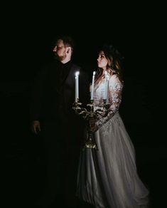 a man and woman standing next to each other holding candles